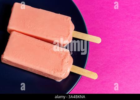 Eis von schwarzen Beeren, die auf blauem Schälchen und Fuchsia-Hintergrund schmelzen. Leerzeichen Stockfoto