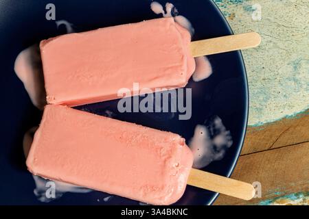 Eis aus schwarzen Beeren, die auf blauem Schälchen und farbenfrohem Hintergrund schmelzen. Stockfoto