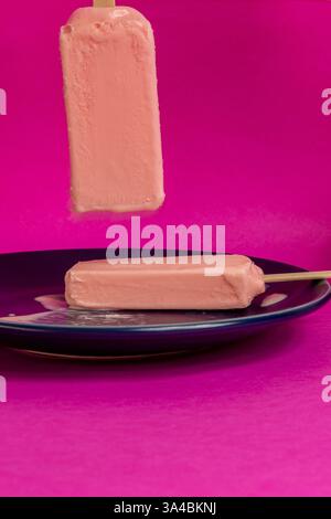 Eis von schwarzen Beeren, die auf blauem Schälchen und Fuchsia-Hintergrund schmelzen. Leerzeichen Stockfoto