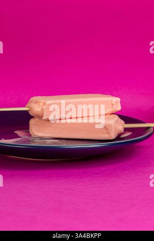 Eis von schwarzen Beeren, die auf blauem Schälchen und Fuchsia-Hintergrund schmelzen. Leerzeichen Stockfoto