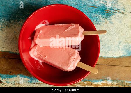 Eis aus schwarzen Beeren, die auf roter Schüssel und farbenfrohem Hintergrund schmelzen. Leerzeichen Stockfoto