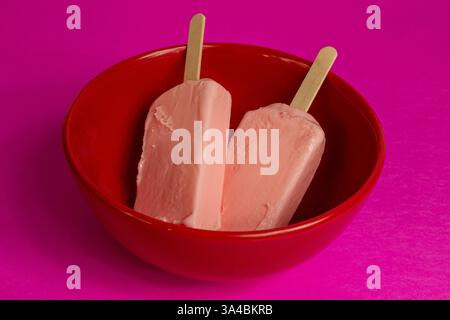 Eis von schwarzen Beeren, die auf rotem Schüssel und Fuchsia-Hintergrund schmelzen. Stockfoto