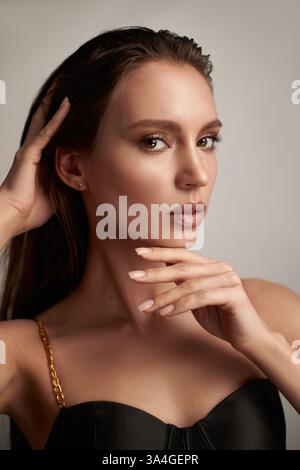 Das Model mit langen Haaren zeigt sich selbstbewusst in einem stilvollen schwarzen Outfit. Mit den Händen wird das Gesicht umrahmt, während es ein Gefühl von Pose und Charme ausstrahlt Stockfoto