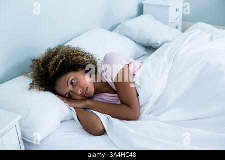 Afroamerikanerin, die im Bett liegt und zu Hause nachdenklich und entspannt aussieht Stockfoto