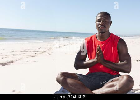 Meditation am Strand, Afroamerikaner in rotem Hemd genießt friedlichen Moment, Kopierraum Stockfoto