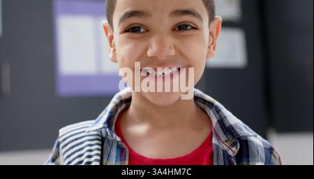 Lächelnder Junge im Klassenzimmer mit kariertem Hemd und rotem T-Shirt Stockfoto