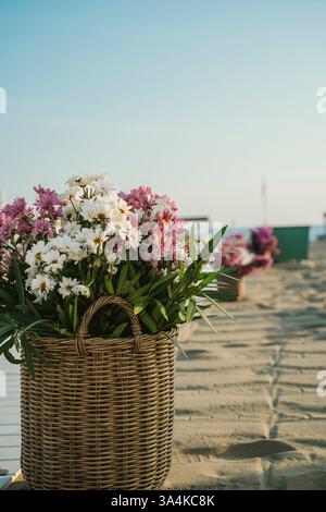 Ein Korb mit leuchtenden weißen und violetten Blumen an einem Sandstrand. Die ruhige Atmosphäre bietet Entspannung und Ruhe im Hotel Stockfoto