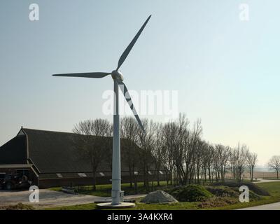 10. März 2025 - Groningen-Niederlande: In der Nähe eines traditionellen niederländischen Bauernhofs steht eine kleine Windkraftanlage, die erneuerbare Energie in einer ländlichen Landschaft erzeugt. Stockfoto