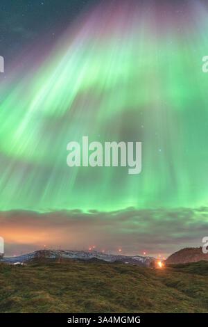 Wunderschöne Aurora Borealis über der Insel Kvaløya, tanzende Nordlichter, die sich in den Gewässern des Nordatlantiks spiegeln, grünes Licht am Himmel Stockfoto