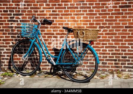 SKAGEN, DÄNEMARK - 1. JUNI 2023 blaues Fahrrad, das an einer roten Ziegelmauer mit Körben hinten und vorne lehnt Stockfoto