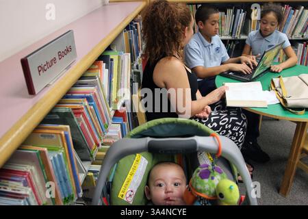 8. Oktober 2014 - Miami Gardens, FL, USA - Homestead Mutter, Christina Morua, 28, Zentrum, hilft ihren Kindern, Abel Martinez, 11, und Alina Martinez, 9, TOP, Sebastian Roman spielt in seinem Kinderwagen in der South Regional Library am 10. Oktober 2014 in Cultler Bay, Fla. Morua ist einer von vielen Eltern, die auf Bibliotheken angewiesen sind, um die Online-Hausaufgaben ihrer Kinder zu erledigen. (Abbildung: © Jon Durr/TNS/ZUMA Wire) Stockfoto