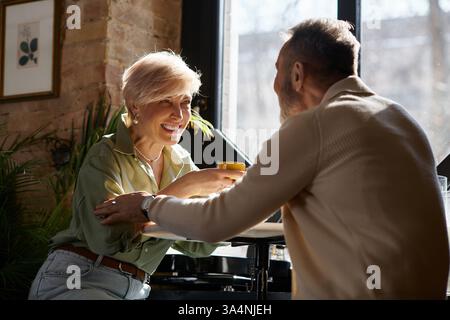Ein fröhliches Paar lacht bei einem Drink und genießt ihre gemeinsame Zeit im sonnendurchfluteten Café. Stockfoto