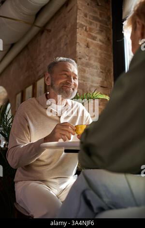 Ein Paar mittleren Alters teilt ein Lächeln und spricht sich bei einem Drink in einem warmen Café. Stockfoto