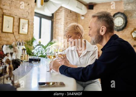Ein Paar mittleren Alters teilt einen intimen Moment in einer eleganten Bar, lacht und trinkt in der Hand. Stockfoto
