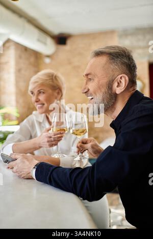Ein Paar mittleren Alters teilt sich Getränke und lächelt in einer gemütlichen Bar. Stockfoto