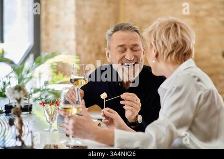 Ein Paar mittleren Alters teilt sich Lachen und leckere Snacks bei einem Drink in einer intimen Umgebung. Stockfoto