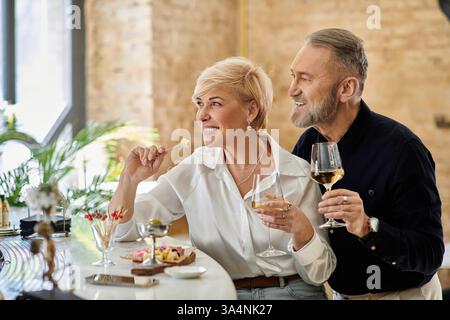 Ein Paar mittleren Alters lacht und trinkt, während es eine köstliche Mahlzeit genießt. Stockfoto