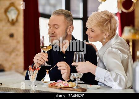 Ein Paar mittleren Alters teilt sich einen intimen Moment bei einem Drink und einer Vorspeise in einer gemütlichen Umgebung. Stockfoto
