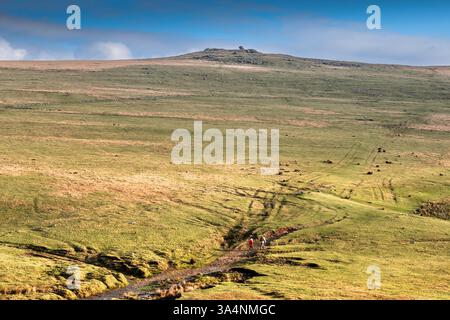 Der Fernblick von zwei Wanderer auf der rauen Strecke, die zum Roughtor Rough Tor auf dem wilden windgepeitschten Bodmin Moor in Cornwall in Großbritannien führt. Stockfoto