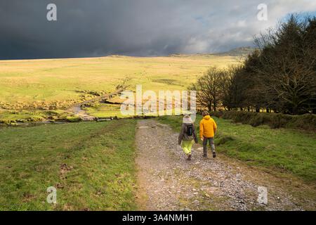 Zwei Personen, die auf einem Pfad in Richtung Roughtor Rough Tor auf dem wilden windgepeitschten Bodmin Moor in Cornwall in Großbritannien spazieren. Stockfoto