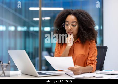 Ernsthaft denkende Finanzierin, die Papierkram im Büro macht. Konzentrierter Buchhalter, der Dokumente und Papiere in der Hand hält. Geschäftsfrau überprüft Daten, arbeitet im Büro. Stockfoto