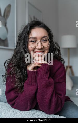 Psychologin, glückliche Mutter sitzt zu Hause und lächelt in einem burgunderroten Pullover in die Kamera Stockfoto