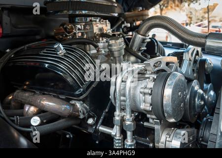 1964 Ford F-100 Fahrzeugmotor mit glänzenden Metallteilen, Schläuchen und einem Klimakompressor im Vordergrund. Stockfoto