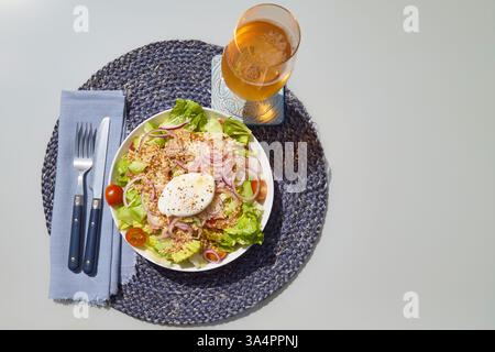 Ein schön angelegter frischer Salat mit knusprigem Salat, Kirschtomaten, roten Zwiebelscheiben, Thunfisch und einem perfekt pochierten Ei, abgeschmeckt mit schwarzem Pfeffer Stockfoto