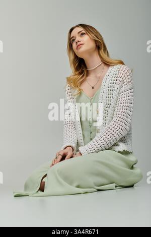 Eine stilvolle junge Frau sitzt anmutig in einem trendigen grünen Outfit und strahlt Frühlingselegantheit aus. Stockfoto