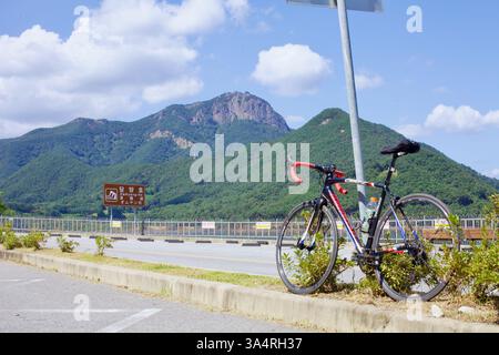 Damyang County, Südkorea - 23. September 2020: Ein Rennrad beugt sich vor einem Wegweiser in der Nähe des Damyang Lake vor der malerischen Kulisse des Jeonggak Mountai Stockfoto