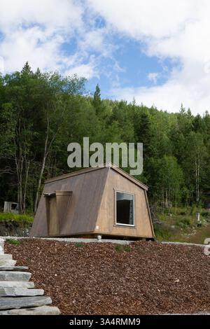 Eine moderne Holzhütte mit eckigem Design befindet sich in einer ruhigen natürlichen Umgebung, umgeben von üppigen grünen Bäumen und einem klaren blauen Himmel, ein umweltfreundliches Hotel Stockfoto