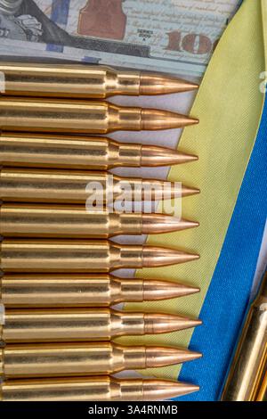 Automatische Gewehrpatronen und ukrainische Flagge auf dem Hintergrund amerikanischer Dollars Stockfoto
