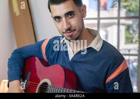 Porträt eines lächelnden jungen Musikers, der in seinem neu eingezogenen Haus Gitarre spielt Stockfoto