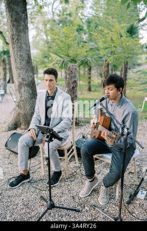 Austin, Texas, USA – 15. April 2024: Gitarrist singt in ein Mikrofon, während er neben einem Sänger auf Stühlen im Park Gitarre spielt Stockfoto