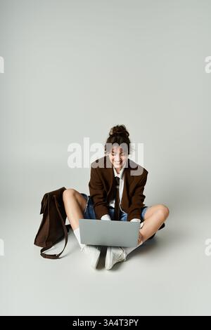 Charmante junge Dame in modischem Outfit greift gerne aus einer gemütlichen Position mit ihrem Laptop in Berührung. Stockfoto