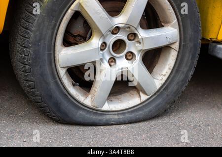 Ein hellgelbes Auto hat leider einen Platten Reifen, der sofort aufgepasst werden muss, um wieder sicher zu fahren Stockfoto