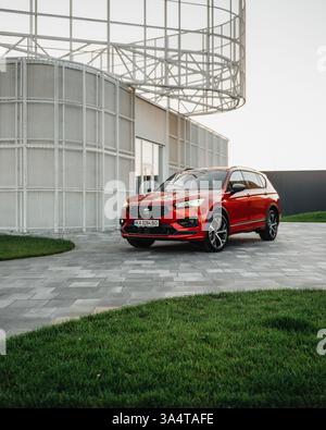 Red SEAT Tarraco parkt in der Nähe des modernen weißen Gebäudes. Vorderansicht des Familien-SUV auf gefliester Einfahrt. Stockfoto