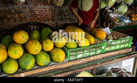 Frische Papayas werden an einem Marktstand mit einem Verkäufer ausgestellt, der Obst in yogyakarta, indonesien, zubereitet Stockfoto