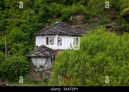Ein rustikales Haus mit einem einzigartigen Steindach liegt vor einem Hintergrund von lebhaftem Grün und Hügeln. Die ruhige Umgebung unterstreicht die Schönheit der Natur und Stockfoto