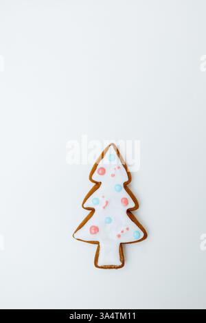 Ein skurriler Lebkuchenkeks in Form eines Weihnachtsbaumes steht auf einem schlichten Hintergrund. Weiß mattiert mit bunten Punkten, ist dieses festliche Leckerli capt Stockfoto