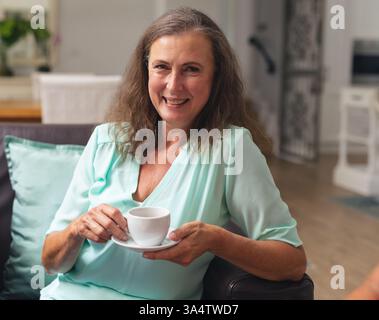 Lächelnde Frau, die zu Hause Kaffee genießt, sich auf einem bequemen Sofa entspannt Stockfoto