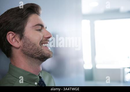 Lächelnder Mann in grünem Hemd, der sich an die Wand lehnt in einem modernen Büro, Kopierraum Stockfoto