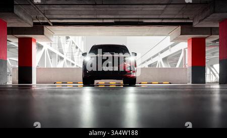 Roter Geländewagen in leerem Parkhaus auf mehreren Ebenen. Vorderansicht des SEAT Tarraco, der zwischen roten Säulen geparkt ist und die Scheinwerfer eingeschaltet sind. Stockfoto