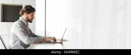 Seitenansicht eines gutaussehenden, reifen Geschäftsmannes, der im Büro arbeitet, einen Laptop benutzt, am Schreibtisch sitzt und Platz für Kopien nutzt Stockfoto