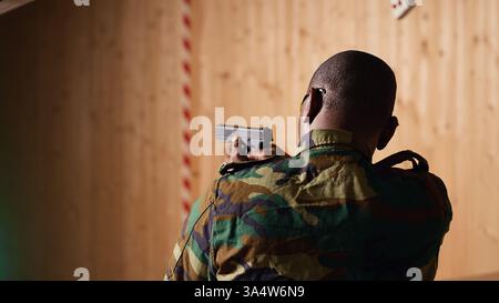 Soldat im Schießstand lädt die Pistole nach, schießt das Ziel und feiert, nachdem er die perfekte Genauigkeit erreicht hat. Militäreinheit im Schießbereich übt Waffen, jubelt nach dem Anschlag auf Bullseye, Kamera B Stockfoto