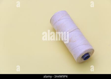 Eine Spule aus weißem Faden auf hellgelbem Hintergrund, von oben betrachtet. Stockfoto