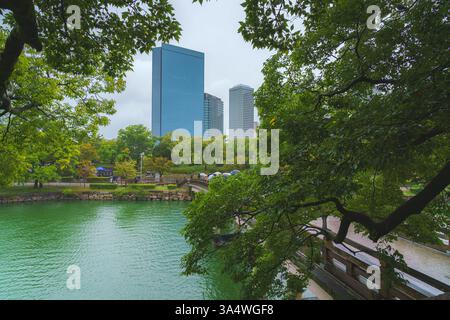 Osaka, Japan - 22. September 2024, Panoramablick durch das Laub der Bäume zu den Wolkenkratzern und der Brücke über den Graben vor der Burg Osaka, Stockfoto