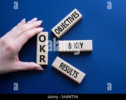 Symbol für OKR-Ziele und wichtige Ergebnisse. Holzblöcke mit den Worten OKR-Ziele und wichtige Ergebnisse. Geschäftsmann Hand. Wunderschöner tiefblauer Hintergrund. Busi Stockfoto