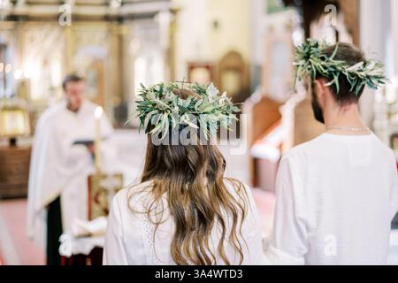 Montenegro, Kotor - 07. Juli 2024: Braut und Bräutigam in Kränzen stehen in der Kirche vor dem Priester, der die Hochzeitszeremonie durchführt Stockfoto