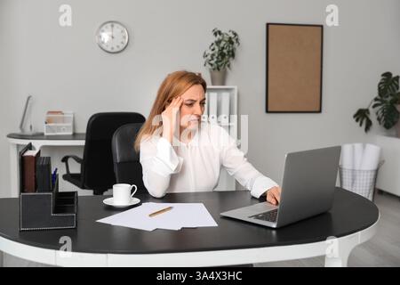Erwachsene Frau mit Kopfschmerzen mit Laptop im Büro Stockfoto